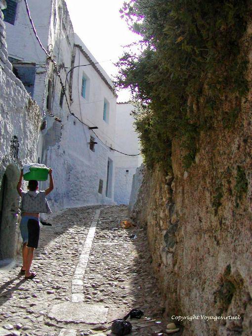 Calçamento de ruas de paralelepípedos e criança que veste a roupa na cabeça, Chefchaouen - Marrocos